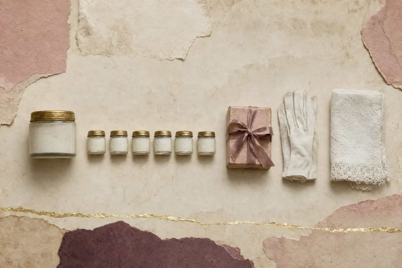 The free sample in objects: a full jar of white face cream beside a row of six tiny sample jars of the same cream, a small gift box tied with ribbon, a white cotton glove and a folded lace-edged towel.