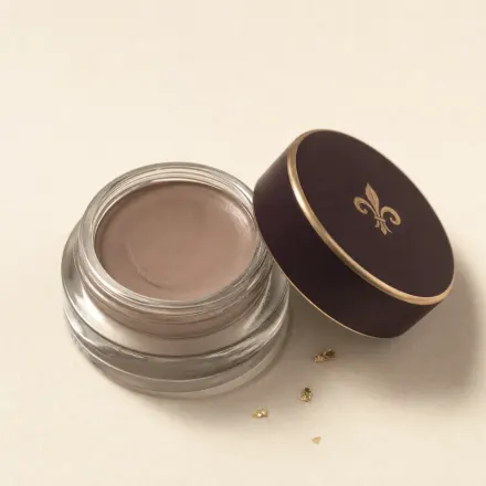 A tiny open glass pot of taupe cream eye base.