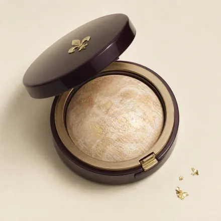 An open compact of domed, marbled pale gold baked highlighter.