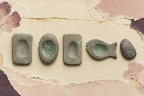 Four Predynastic Egyptian grinding palettes of grey-green siltstone, three plain and one carved as a fish, each worn into a shallow hollow at the centre, with a grinding pebble and green malachite residue.