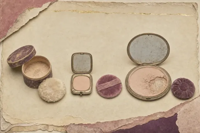 A 1930s powder compact of the wide, flat Flapjack type, a disc about the width of a hand and twice the size of the compacts before it, in gilded metal with a ring-turned lid, its large mirror clouded with age.