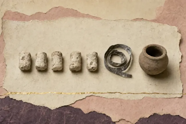 Five small irregular white pellets of compacted lead white laid in a row beside a coiled strip of corroded lead and a small plain Greek pot.