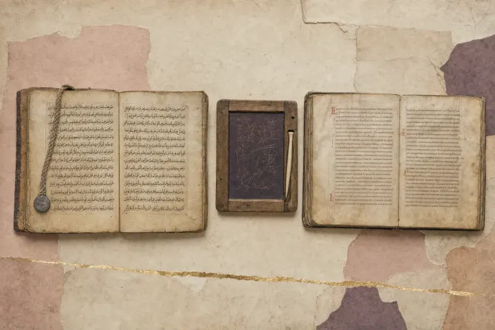 Two open manuscripts side by side on a desk — one in Arabic script, one in Latin minuscule — with a wax tablet of working notes and a stylus between them.