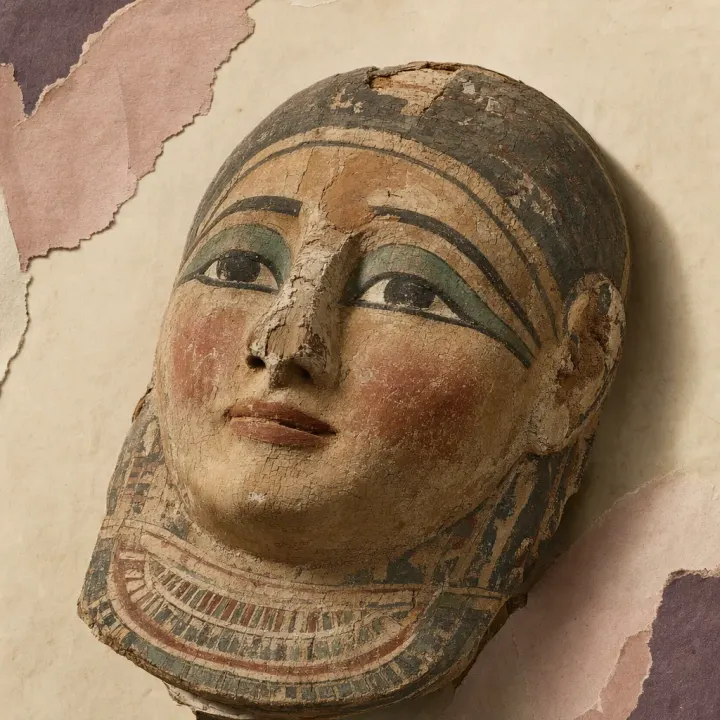 The painted face of an Egyptian coffin lid, carved wood under a finely cracked white ground: long black lines drawn round the eyes, green on the lids and red on the mouth, the paint rubbed to bare wood along the nose.